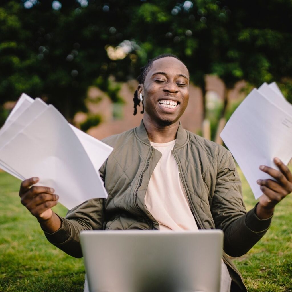 Smiling Student with papers in Hand and computer on his lap