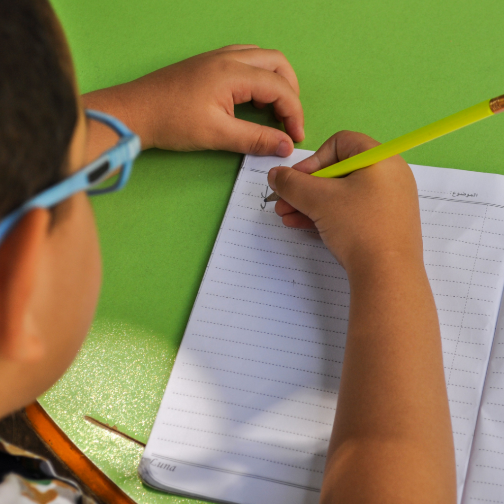 Four Tips for Success With EIW's Homeschool Writing Curriculum 2 a kid with blue glasses writing with a yellow pencil