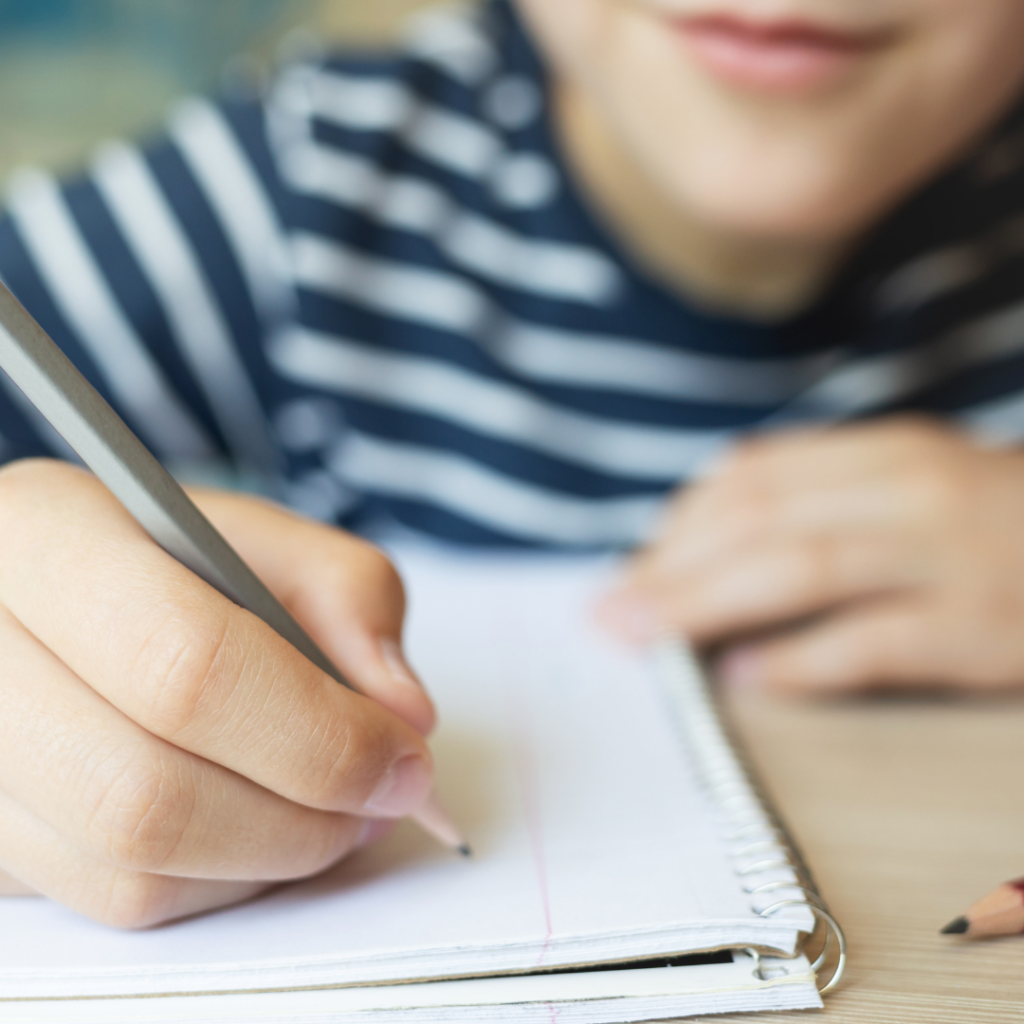 Four Tips for Success With EIW's Homeschool Writing Curriculum 4 a close up of someone holding a pencil, about to write in a notebook